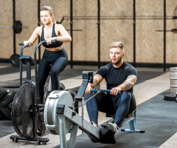 Young couple training on the exercise air bicycle and rowing machine in the gym